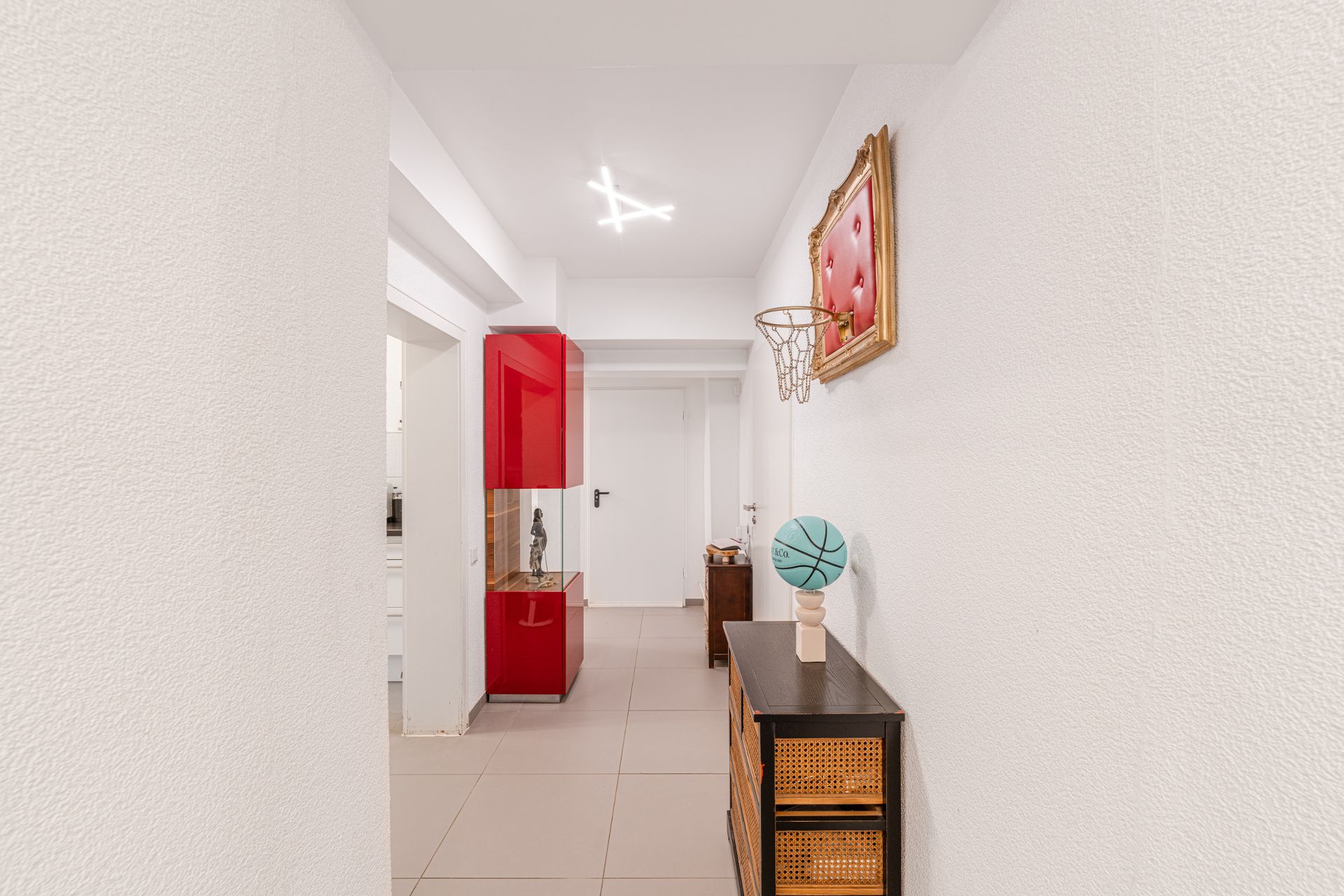 Heller Flur mit Basketballkorb an der Wand, Schrank und rotem Vitrinenschrank.