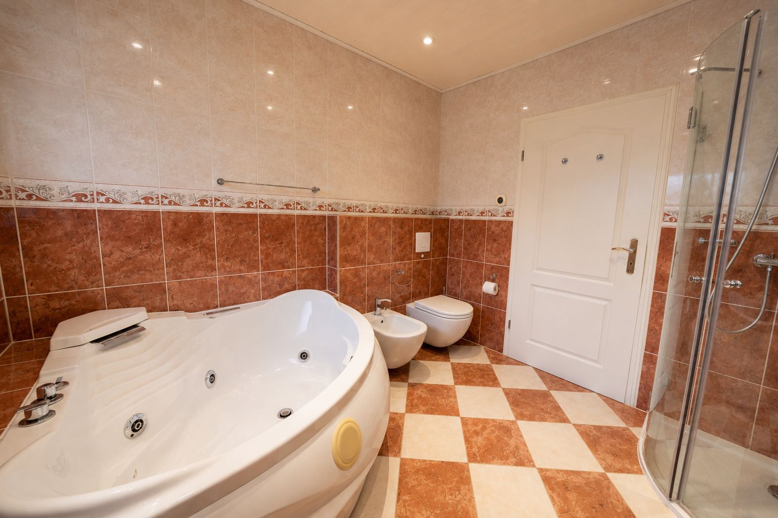 Badezimmer mit Eckbadewanne, Bidet, WC und Duschkabine, Fliesenboden in Schachbrettmuster.