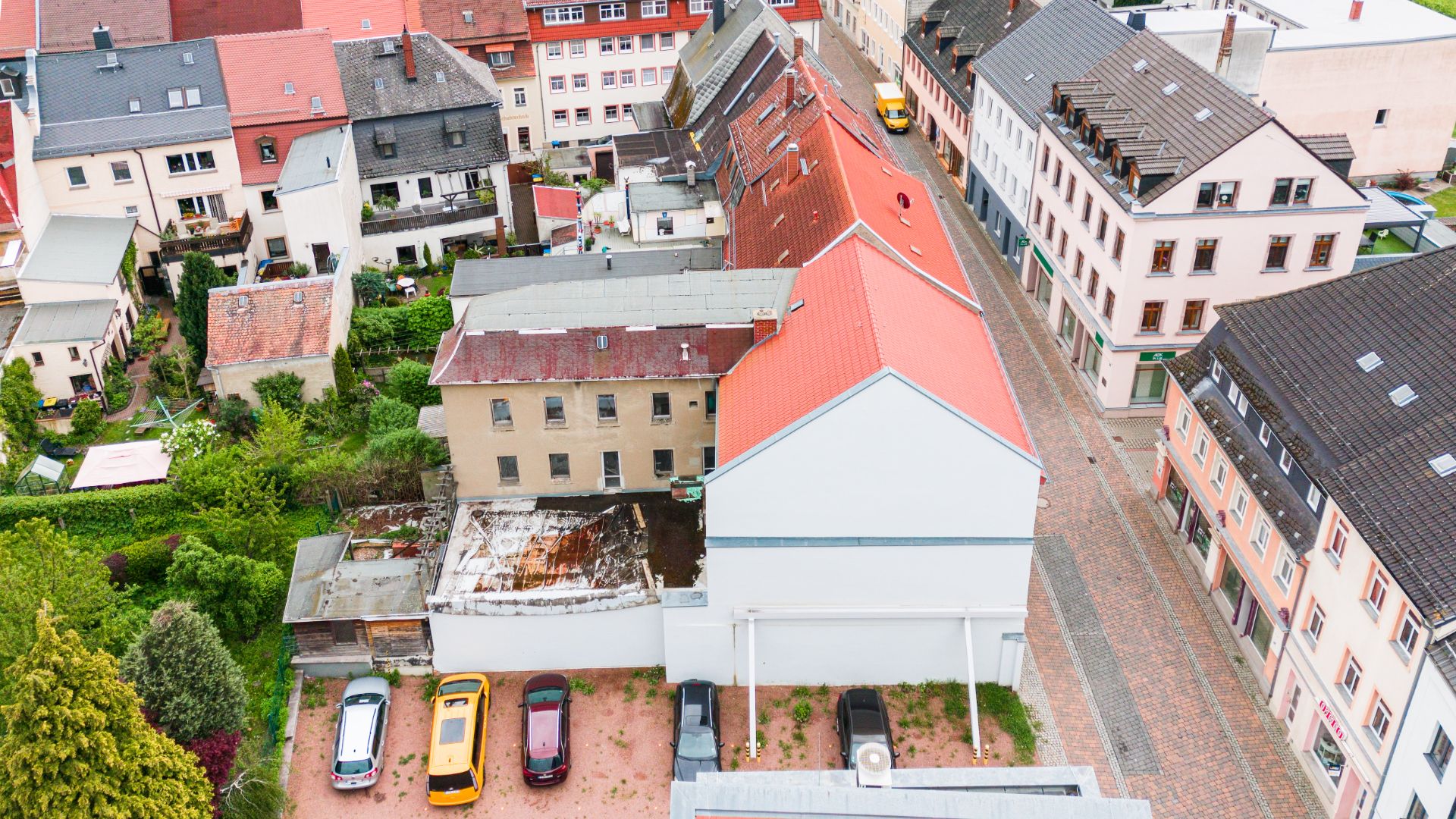 Luftaufnahme mehrerer Wohnhäuser und eines kleinen Parkplatzes mit Autos in einem Wohngebiet.
