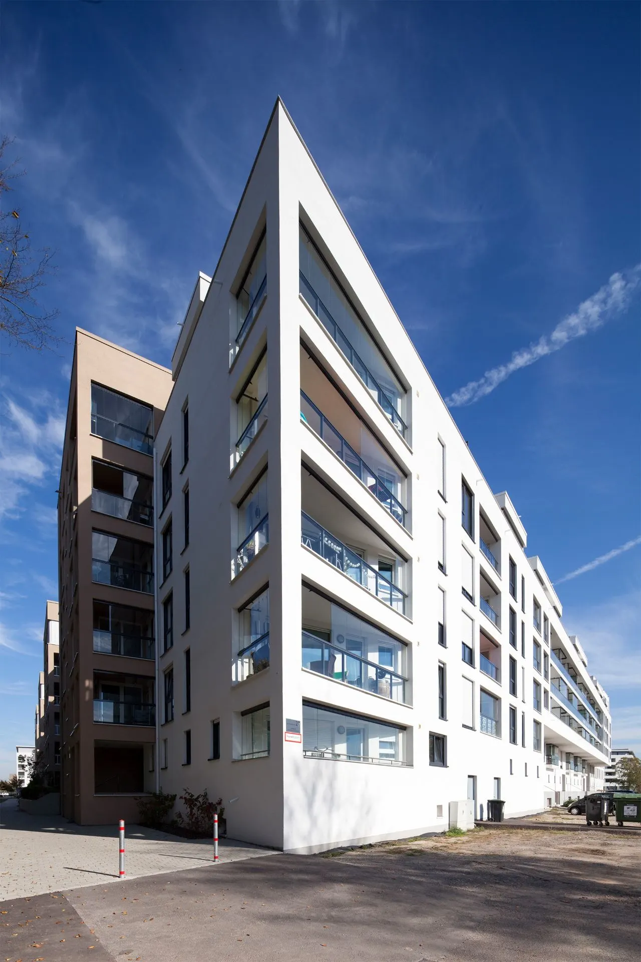 Modernes Wohngebäude mit vielen Balkonen und großen Fenstern an einer Straßenecke.