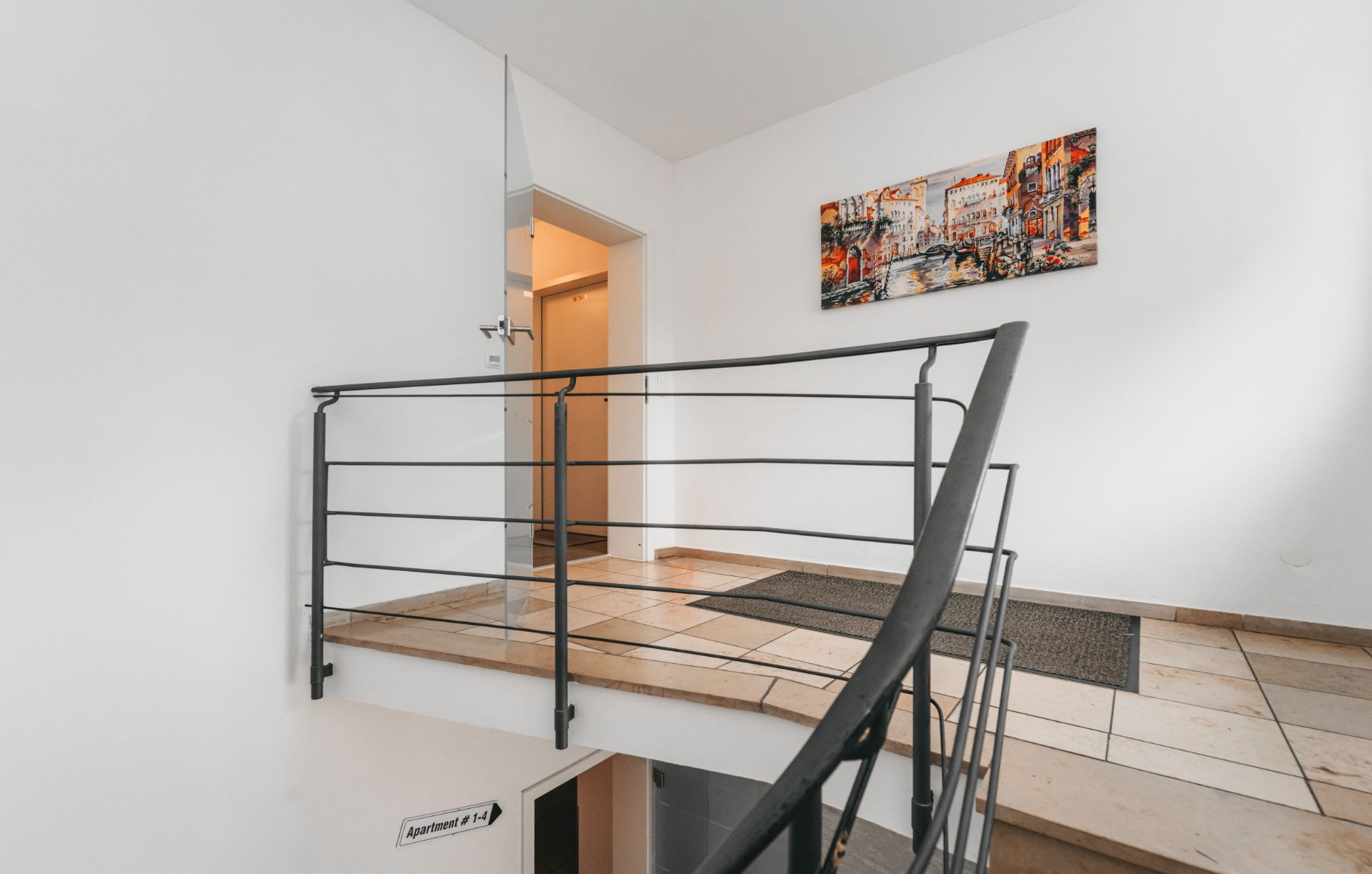 Heller Flur mit Treppengeländer, Eingangstür und buntem Gemälde an der weißen Wand.