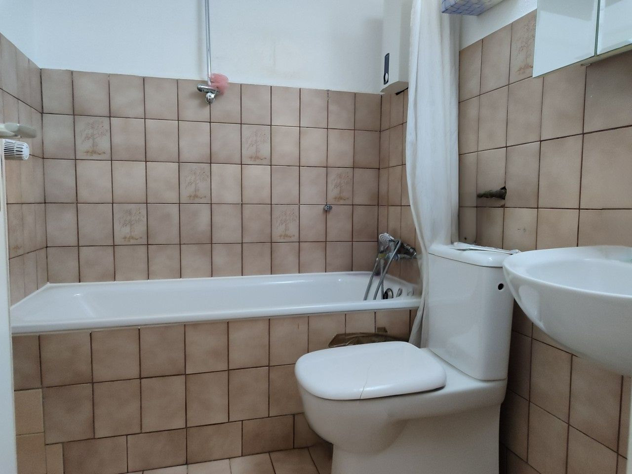 Kleines Badezimmer mit Badewanne, Toilette, Waschbecken und beigen Fliesen an den Wänden.
