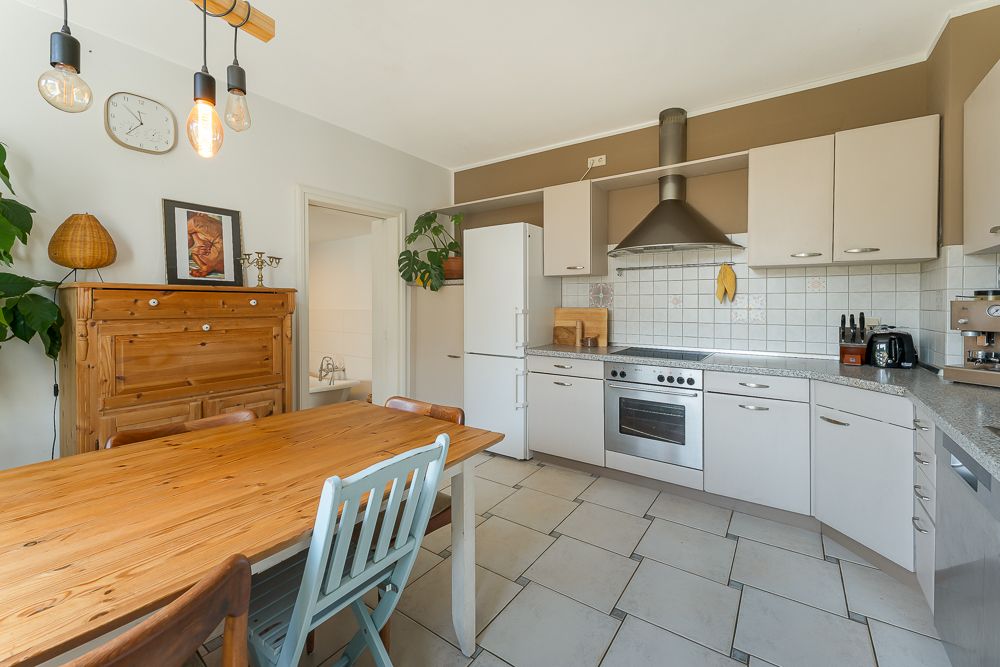 Helle Küche mit Esstisch, Holzschrank, weißen Schränken und modernen Geräten.