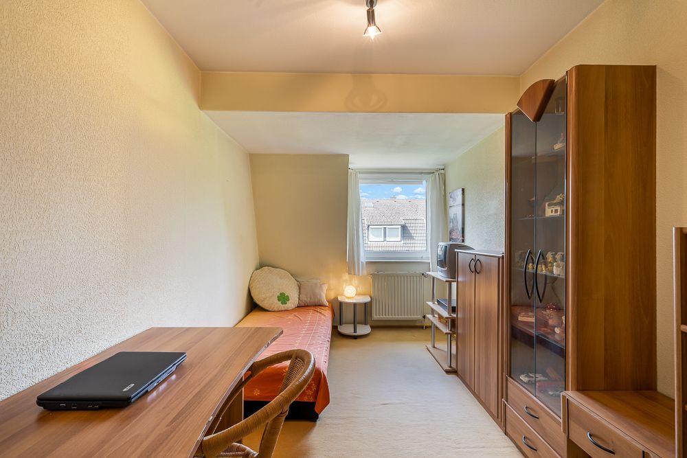 Kleines Zimmer mit Einzelbett, Schreibtisch und Holzschrank, Fenster am Ende des Raums.
