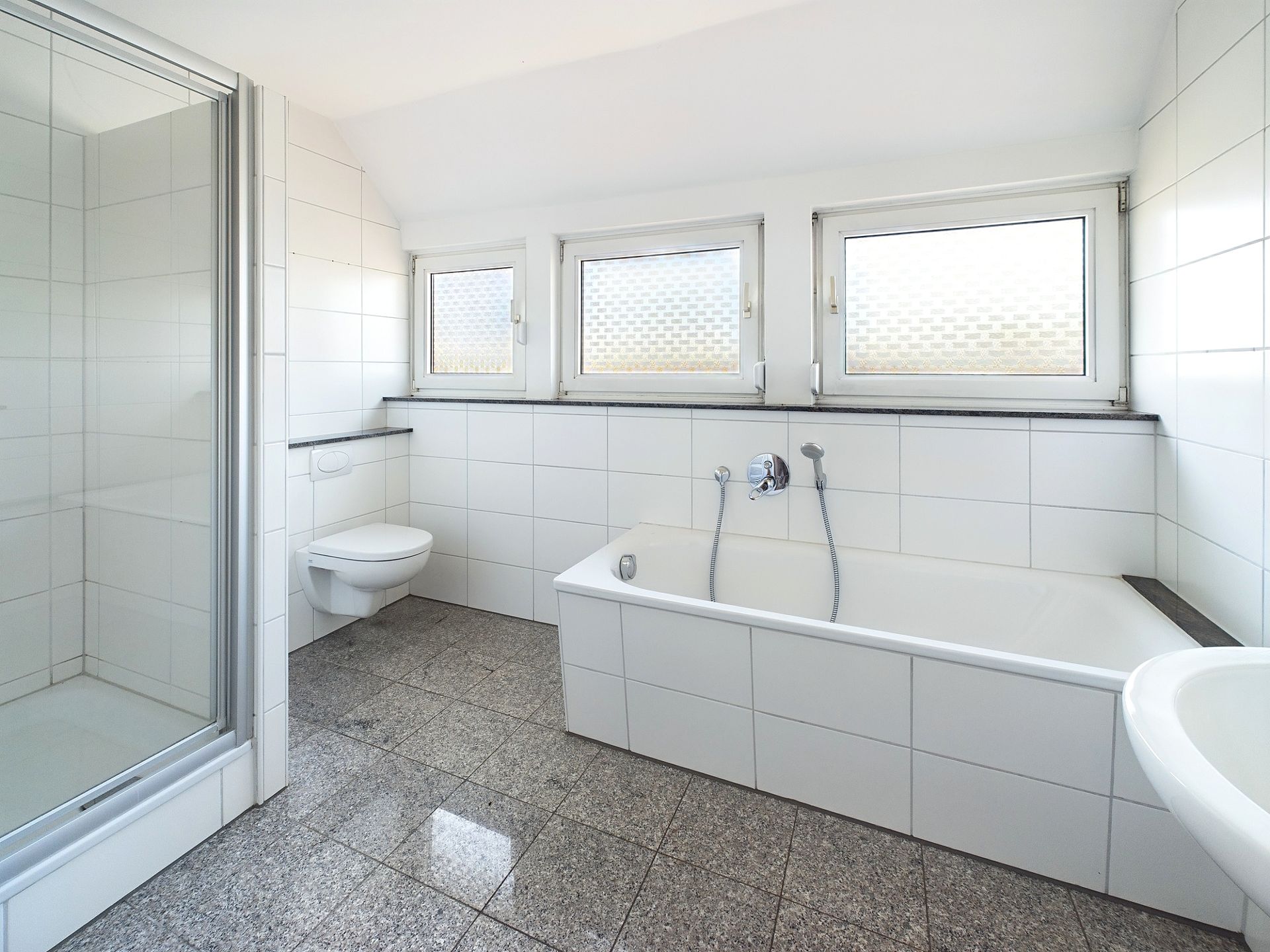 Modernes Badezimmer mit Dusche, Badewanne, WC und drei Fenstern.
