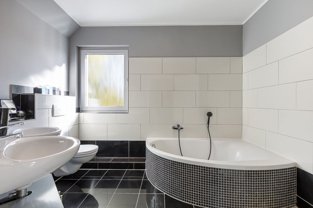 Modernes Badezimmer mit Eckbadewanne, Waschbecken, WC und Fenster.