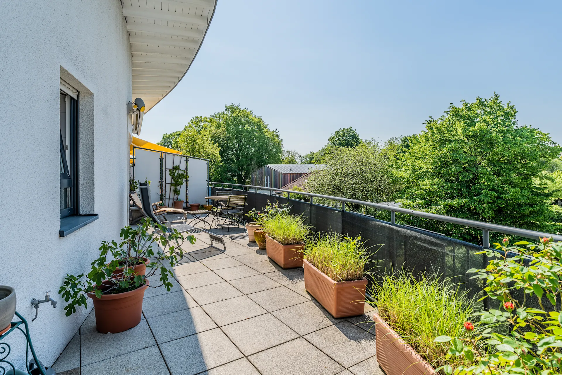 Großer Balkon mit Pflanzenkübeln, Sitzmöbeln und Blick ins Grüne.