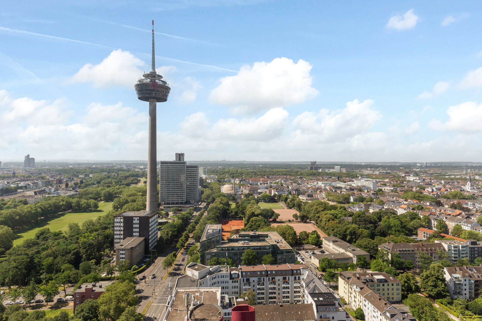 Blick auf eine Stadt mit Fernsehturm und vielen Wohngebäuden, umgeben von Grünflächen.