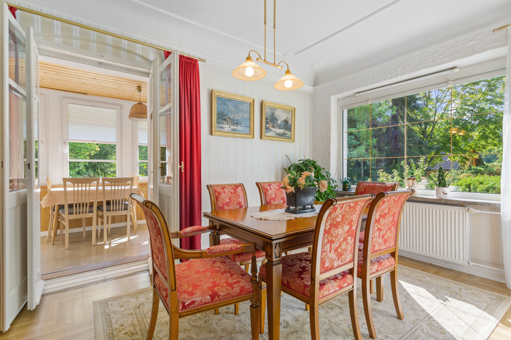 Esszimmer mit Holztisch, sechs roten Stühlen, großem Fenster und Blick in einen zweiten Raum mit Tisch und Stühlen.