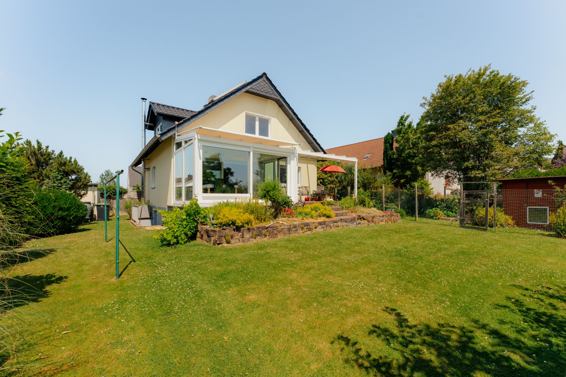 Einfamilienhaus mit Wintergarten und gepflegtem Garten an einem sonnigen Tag.