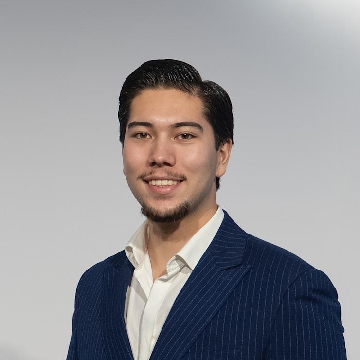 Mann mit kurzem dunklem Haar im blauen Anzug mit weißen Streifen vor hellem Hintergrund.