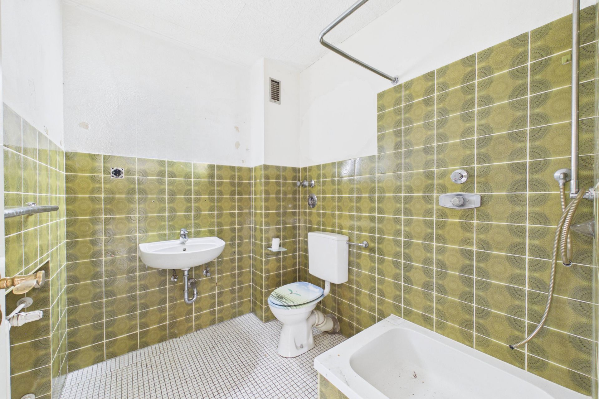 Badezimmer mit grünen Fliesen, Waschbecken, Toilette und Badewanne mit Dusche.