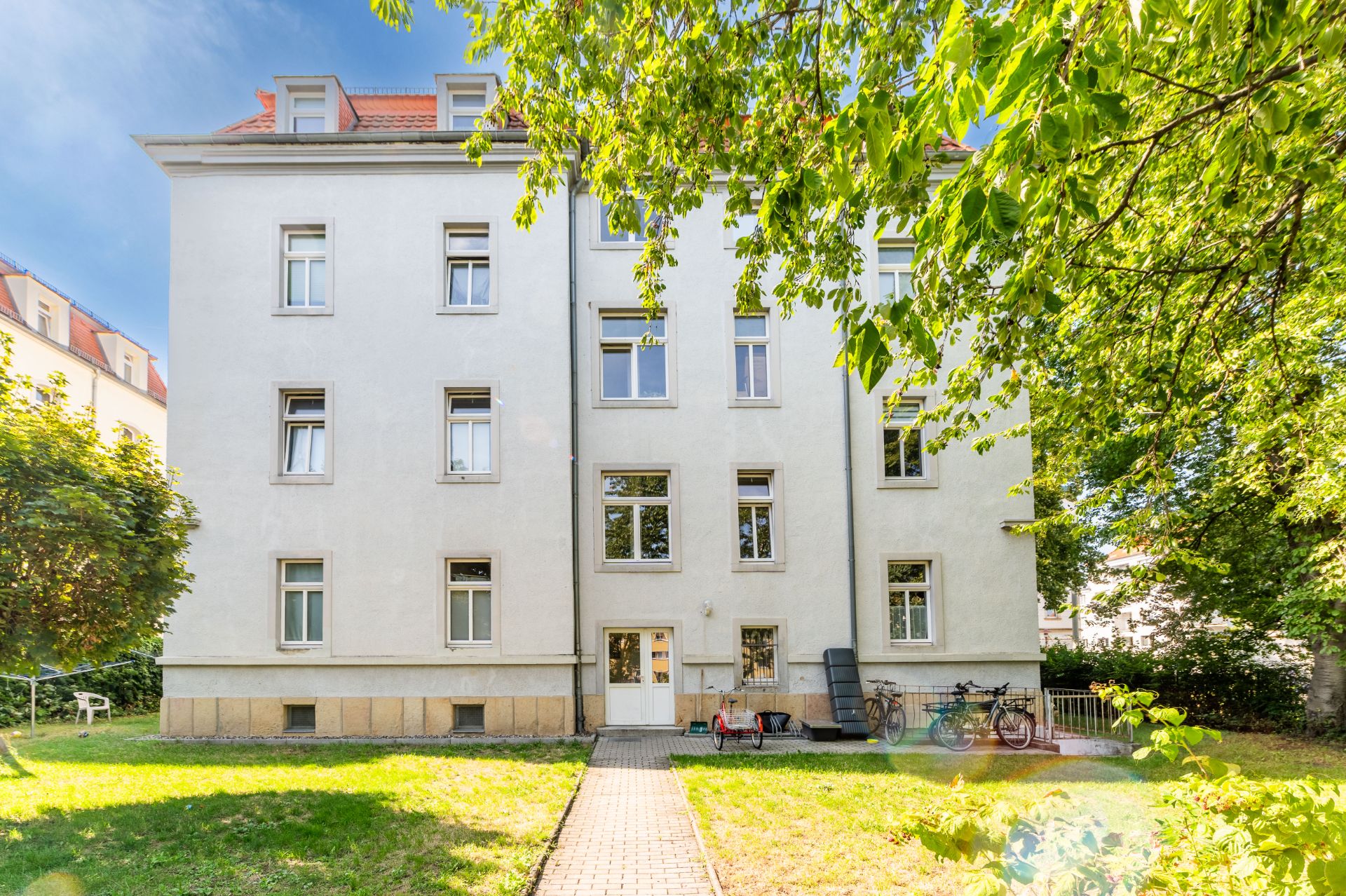 Mehrfamilienhaus mit weißer Fassade, Fahrradständern und Garten im Vordergrund.