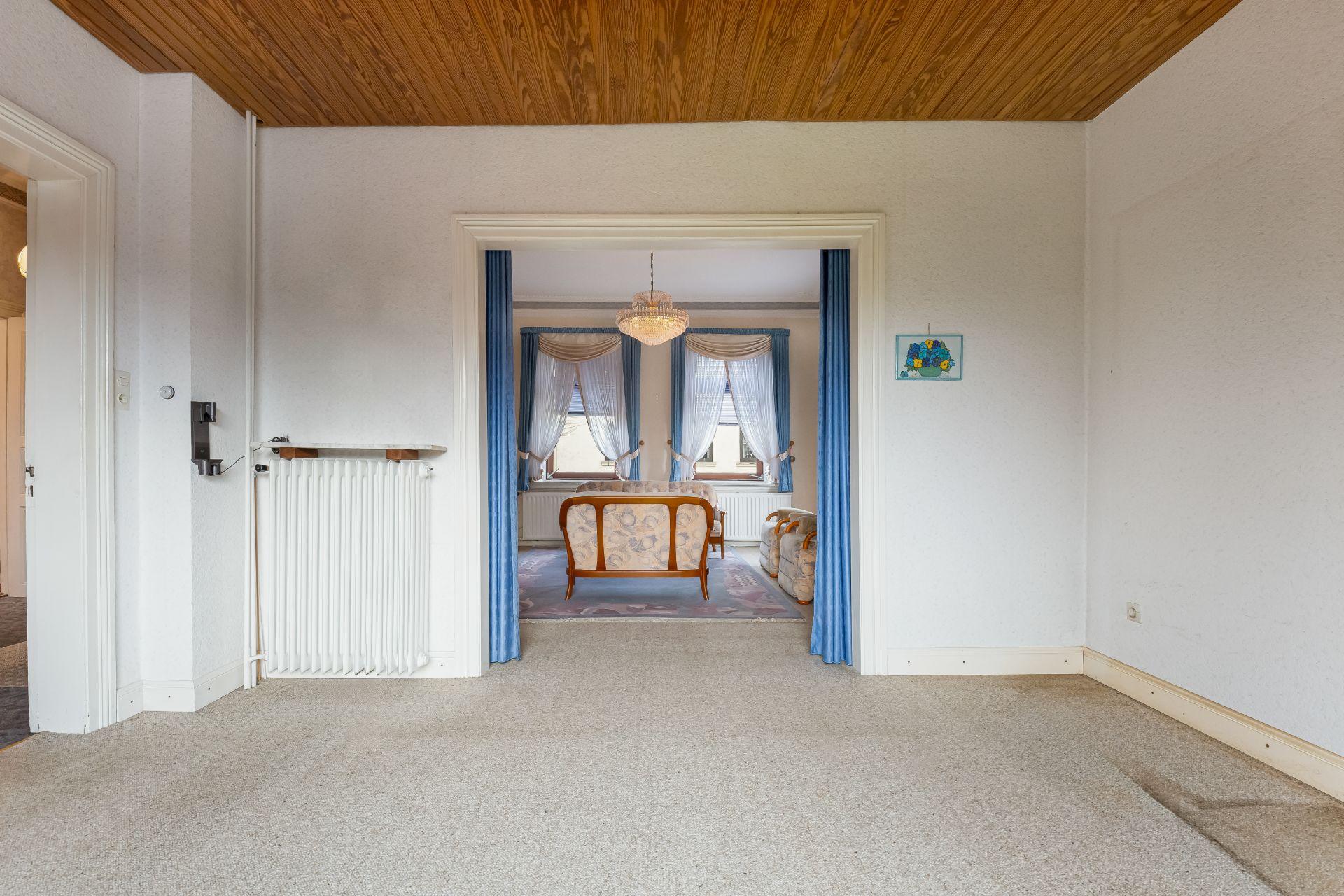 Blick durch offenen Durchgang in ein Wohnzimmer mit Sofa, Sesseln und großen Fenstern.
