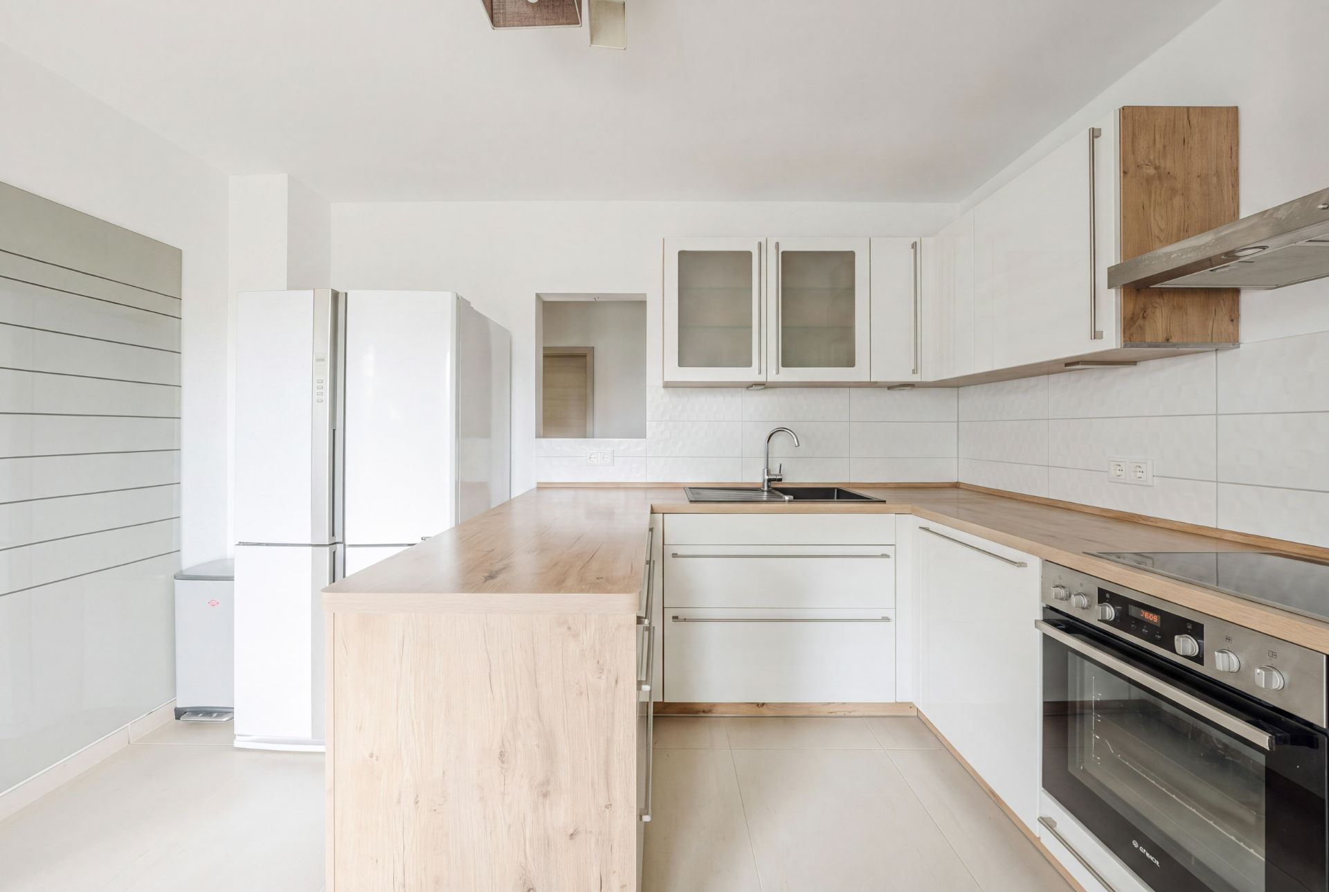 Helle moderne Küche mit Holzarbeitsplatten, weißem Kühlschrank und Einbauherd.