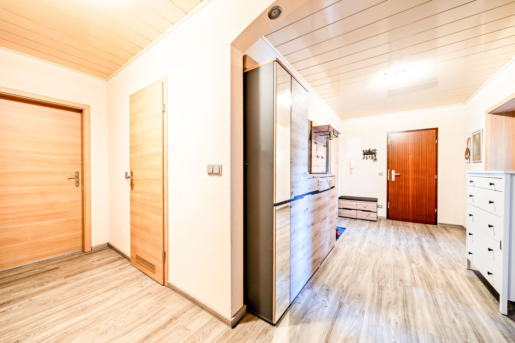 Heller Flur einer Wohnung mit Holztüren, Schränken und Dielenboden.