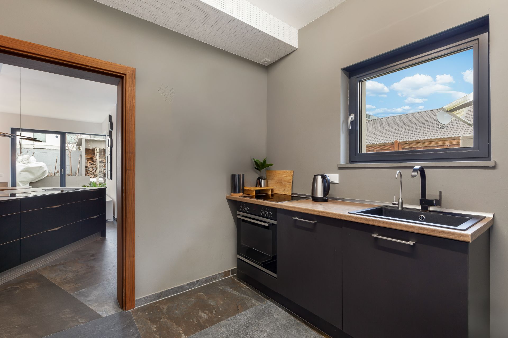 Moderne Küche mit schwarzem Ofen, Spüle, Wasserkocher und Fenster mit Blick nach draußen.