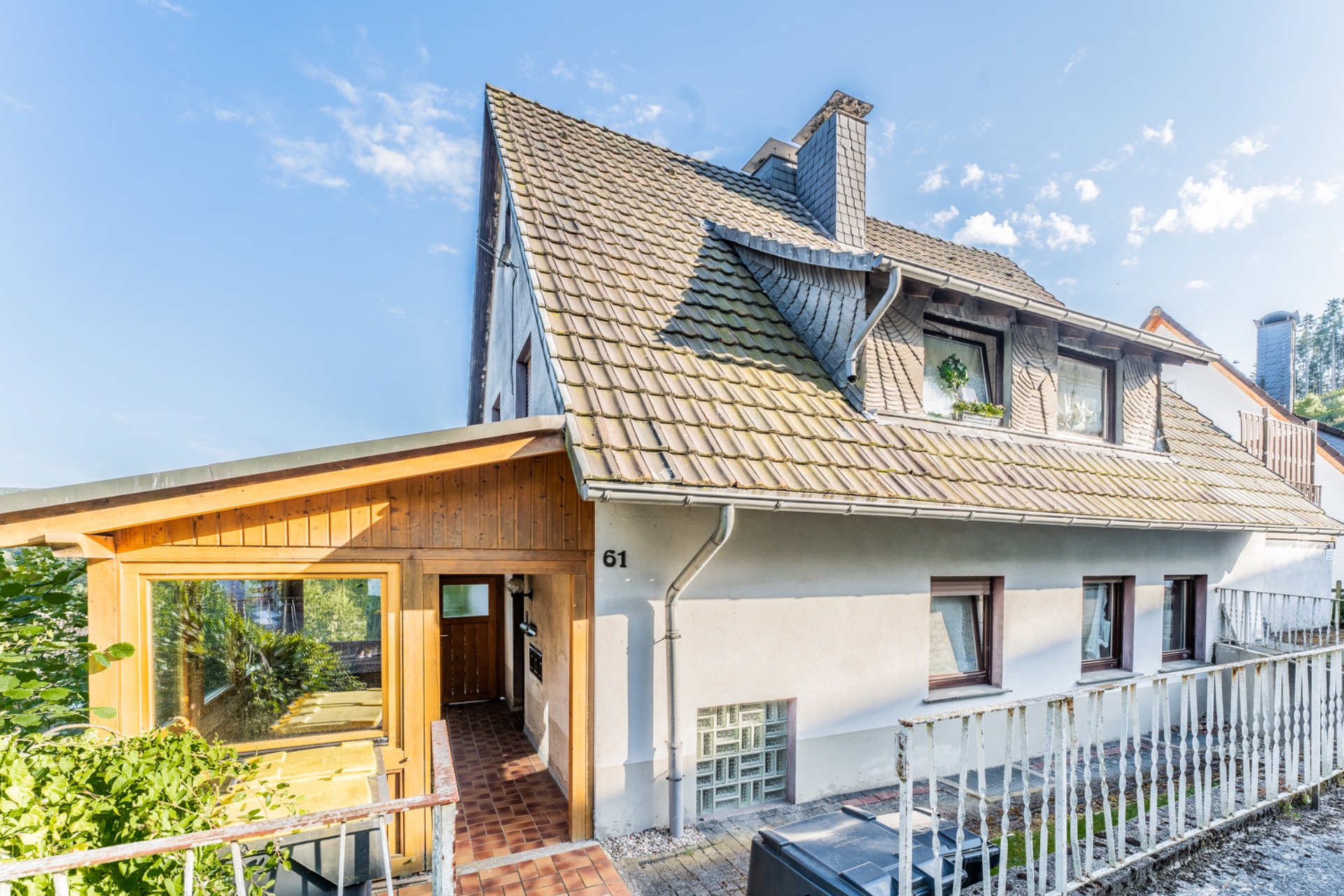 Zweistöckiges Haus mit Schrägdach, Wintergarten und drei Fenstern auf der Vorderseite.