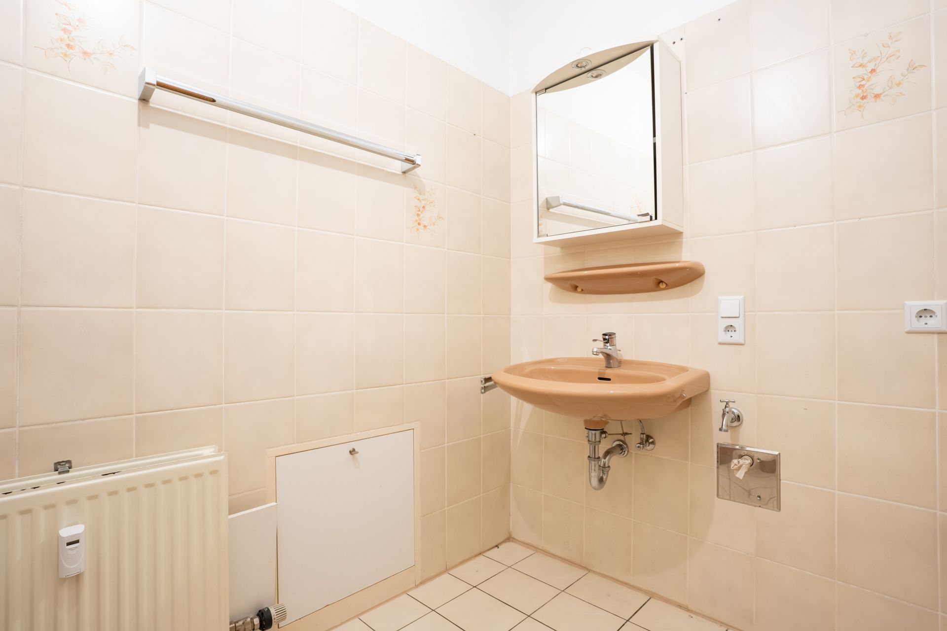 Beiges Badezimmer mit Waschbecken, Spiegel, Regal und Handtuchstange.