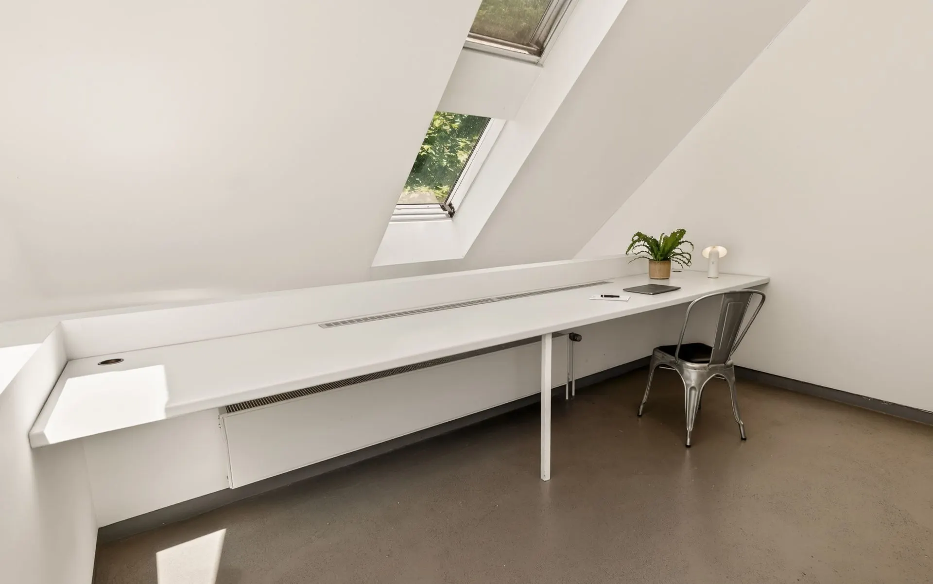 Helles Zimmer mit langem weißen Schreibtisch, Stuhl und Dachfenstern.