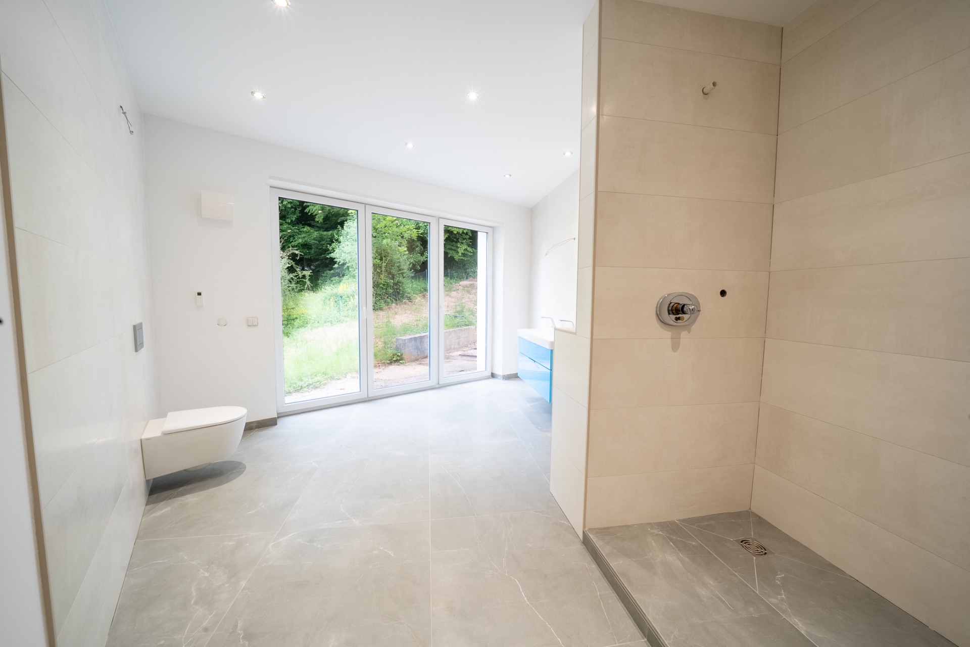 Modernes Badezimmer mit begehbarer Dusche, Toilette und großen Fenstern mit Blick ins Grüne.