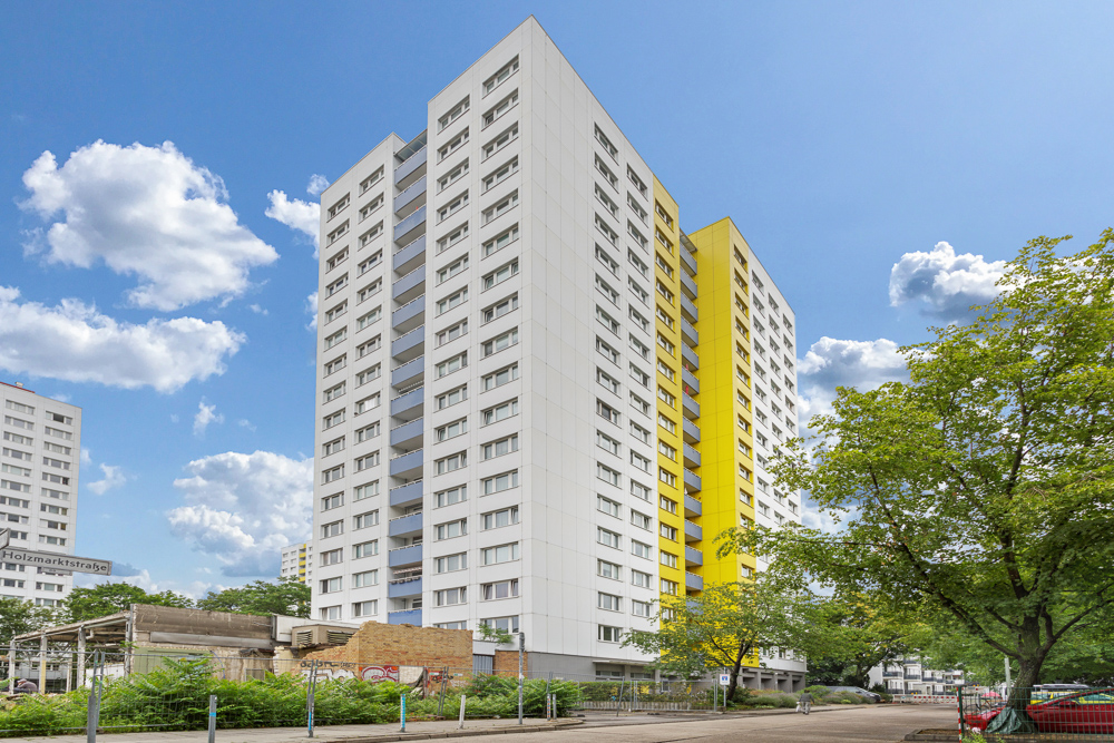 Hohes Wohngebäude mit gelben Elementen, umgeben von Bäumen und Straße.