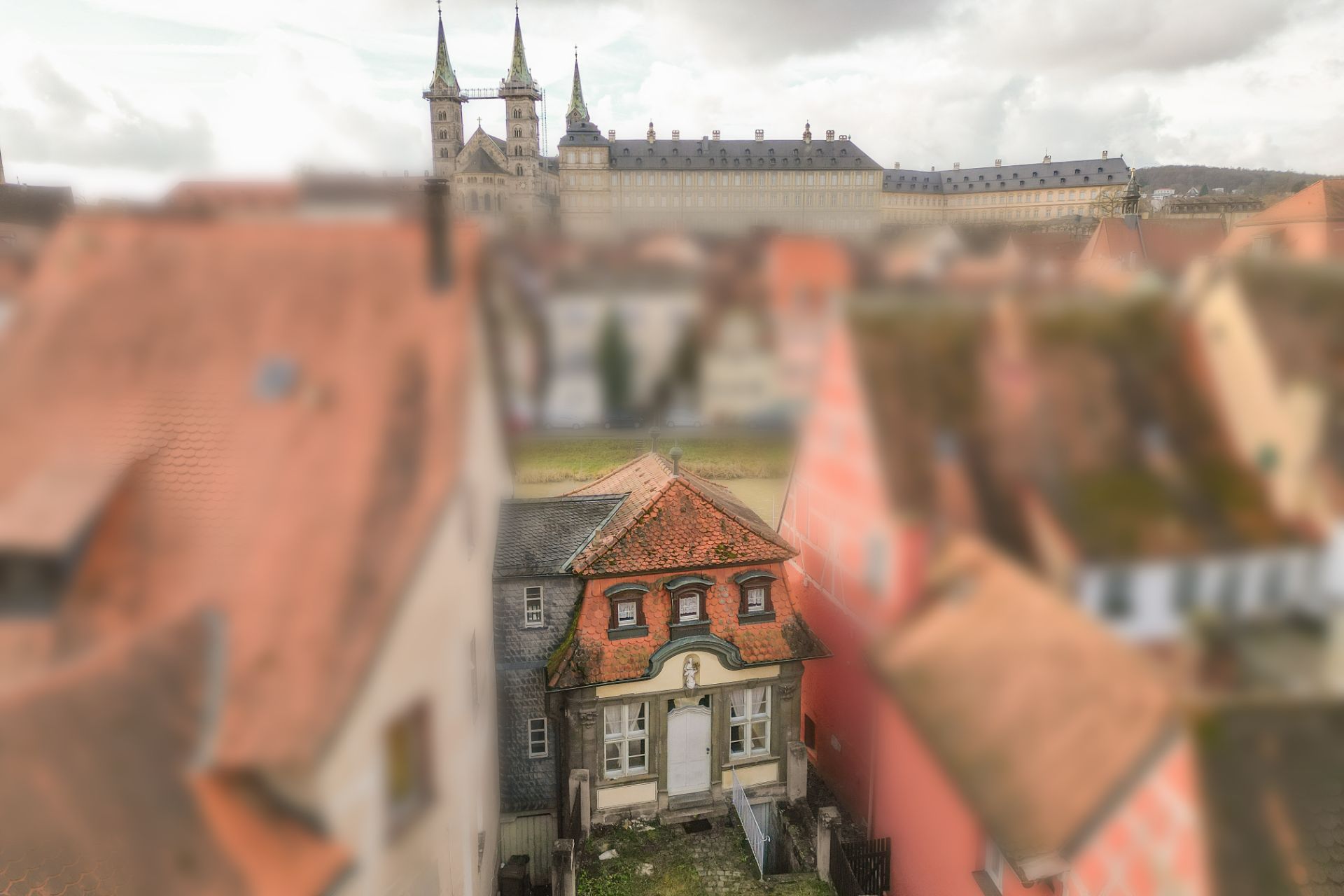 Kleines Haus mit rotem Dach inmitten anderer Häuser, im Hintergrund eine große Kirche.