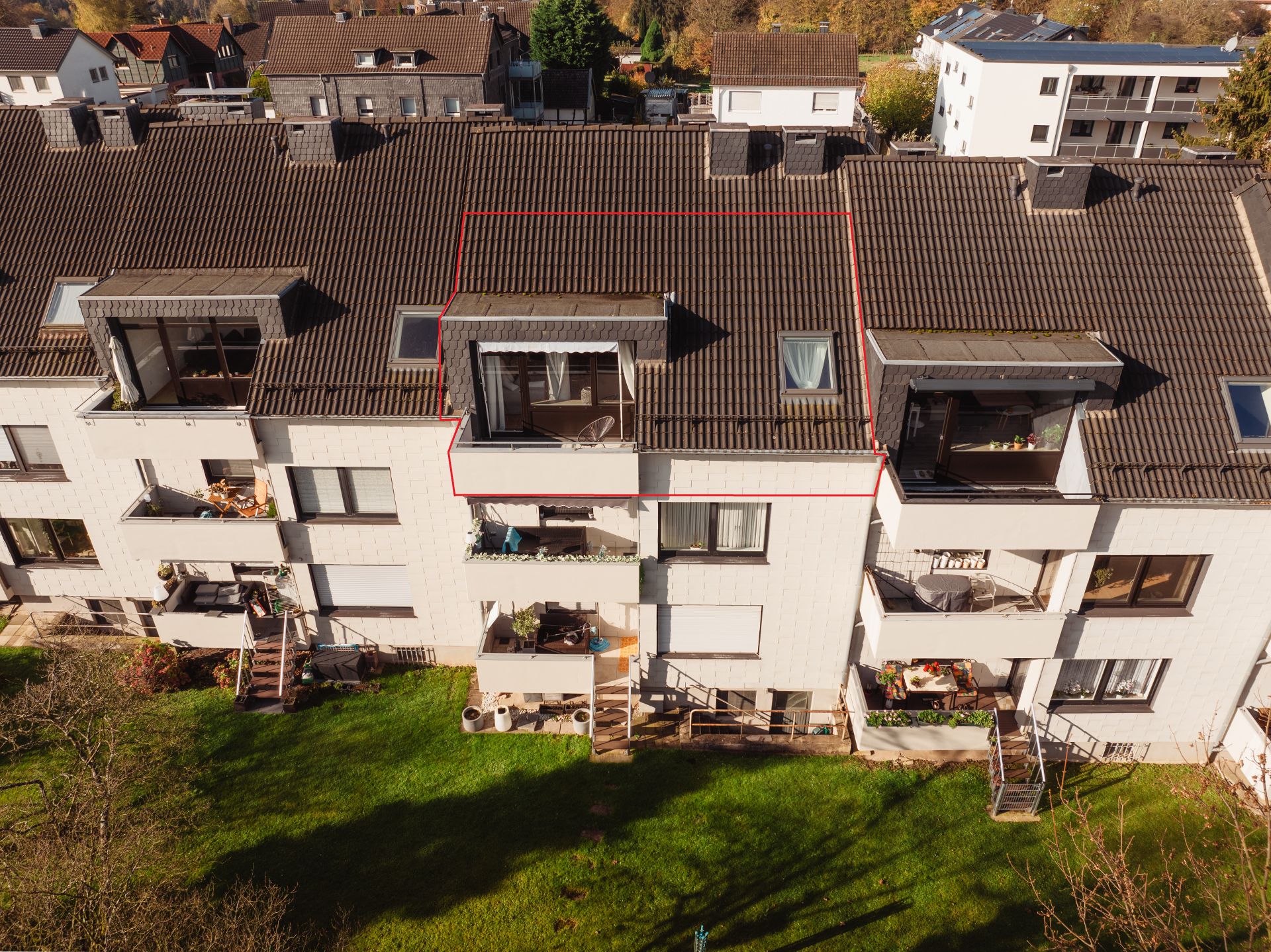 Mehrfamilienhaus mit mehreren Balkonen und Gartenanteil, eine Wohnung ist rot umrandet.