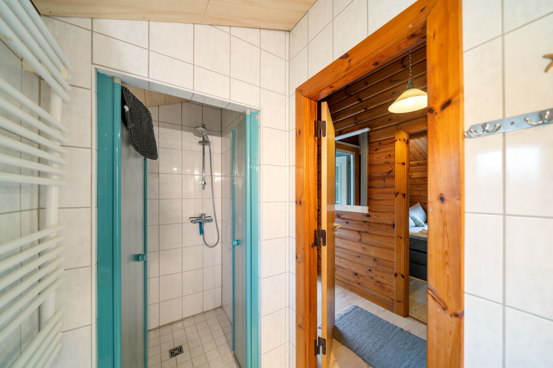 Dusche mit Glastüren und Fliesen, daneben Tür zu holzverkleidetem Raum mit Lampe.