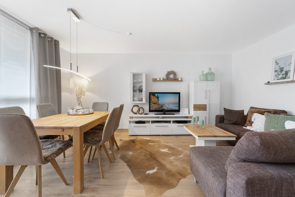 Helles Wohnzimmer mit Essbereich, Holztisch, braunen Sofas und TV auf weißem Möbel.