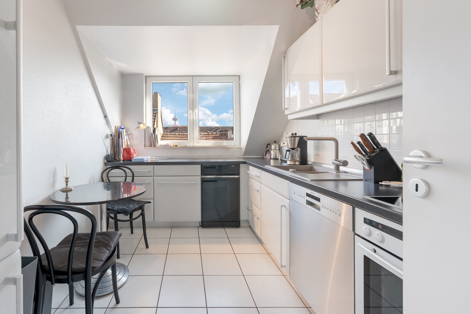 Helle Küche mit weißen Schränken, Esstisch, zwei Stühlen und Fenster mit Ausblick.