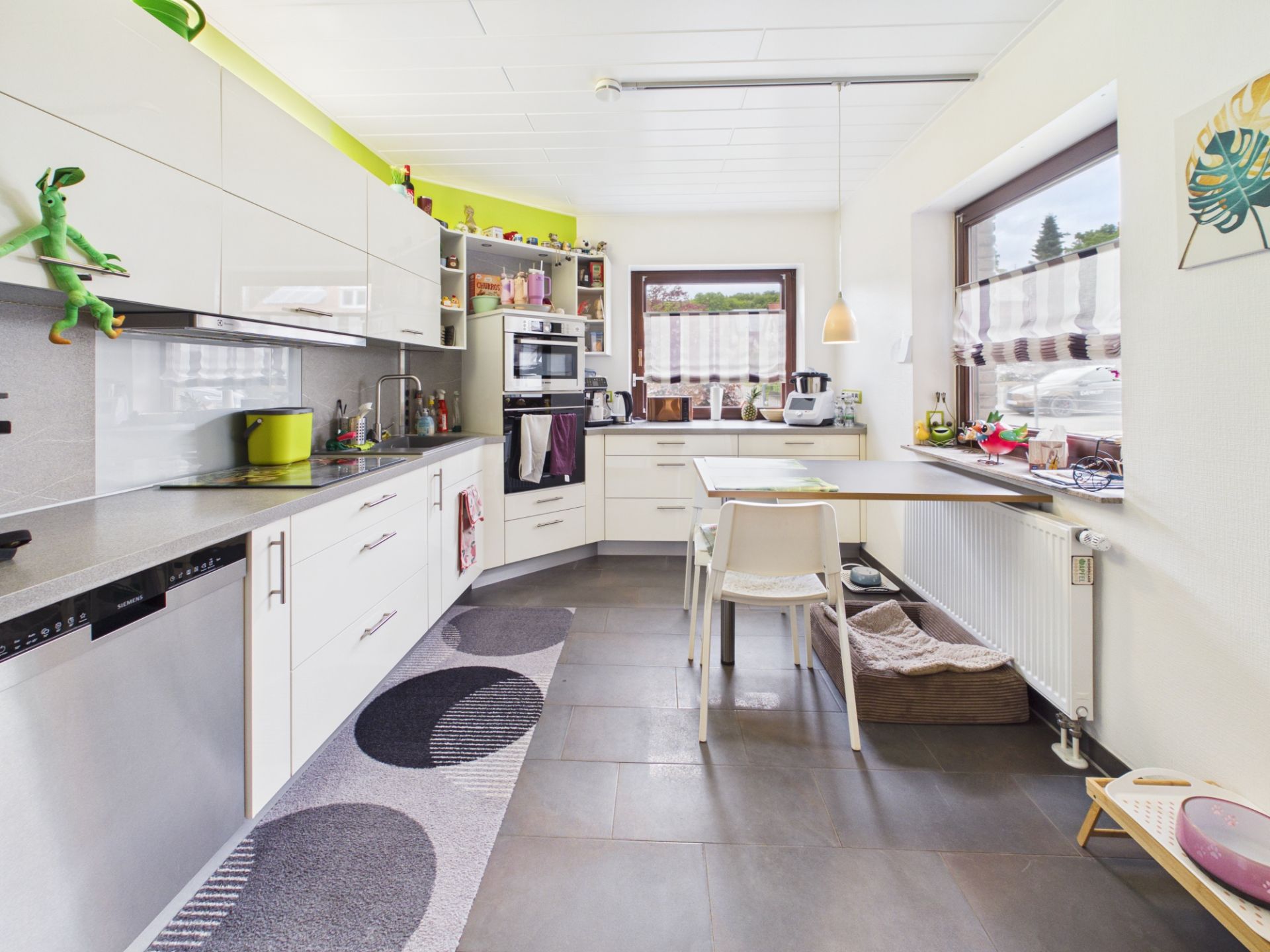 Moderne helle Küche mit weißen Schränken, Essbereich am Fenster und Haustierbett unter dem Tisch.