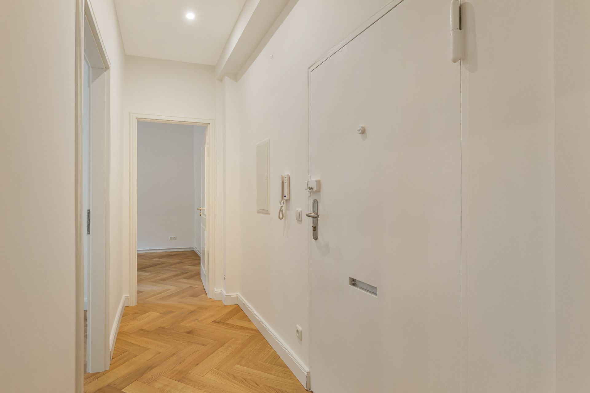 Heller Flur mit Holzboden und weißer Eingangstür in einer Wohnung.