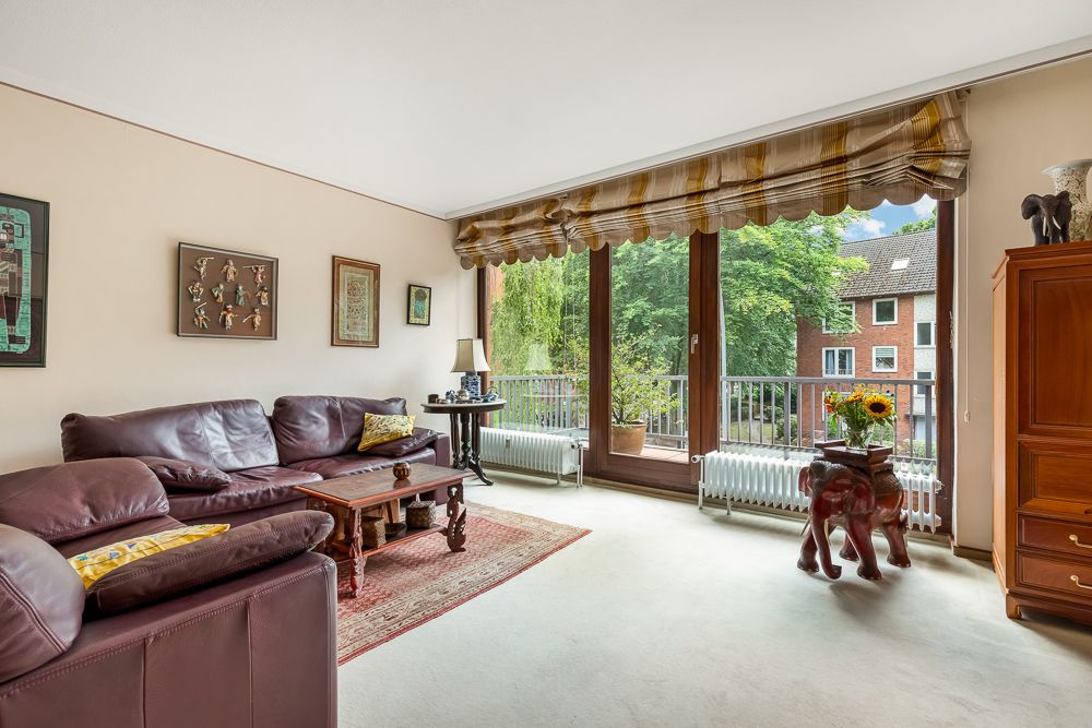 Helles Wohnzimmer mit braunem Ledersofa, Couchtisch, großen Fenstern und Balkonblick.