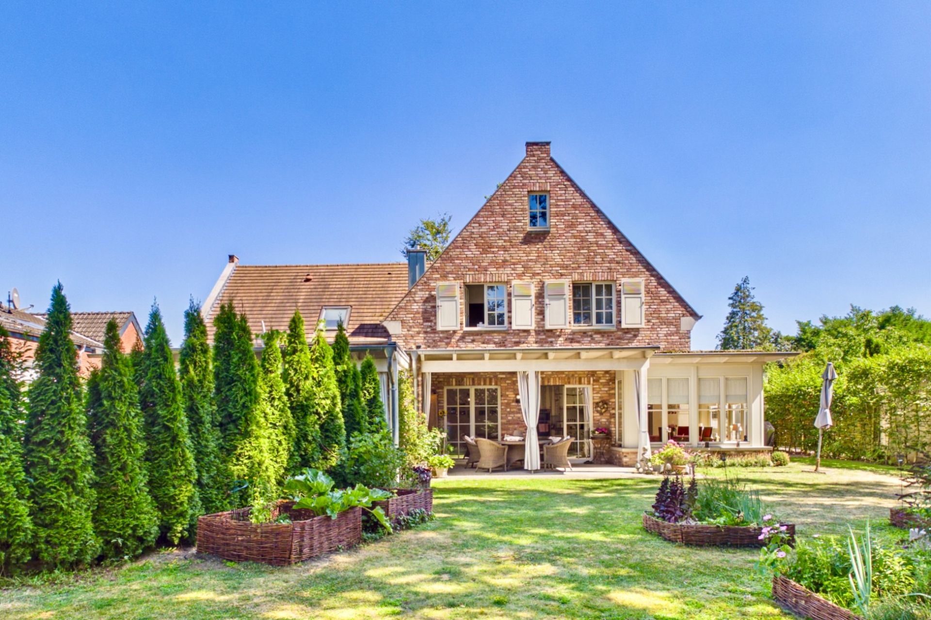 Backsteinwohnhaus mit Terrasse, Gartenmöbeln und gepflegtem Garten mit Hecken und Beeten.