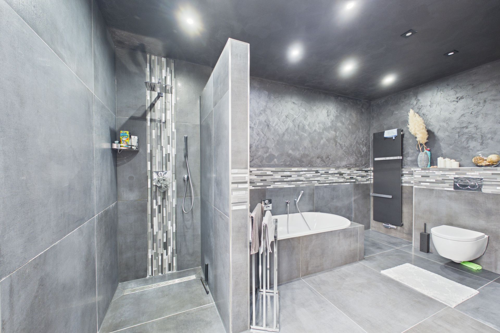 Modernes Badezimmer mit großer Dusche, Badewanne, Wandtoilette und grauen Fliesen.