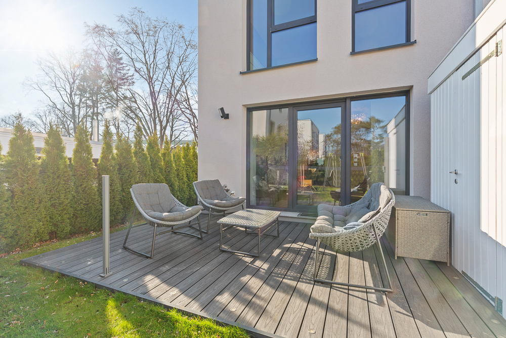 Moderne Terrasse mit Gartenmöbeln, Holzboden und Blick auf einen Garten mit Bäumen.