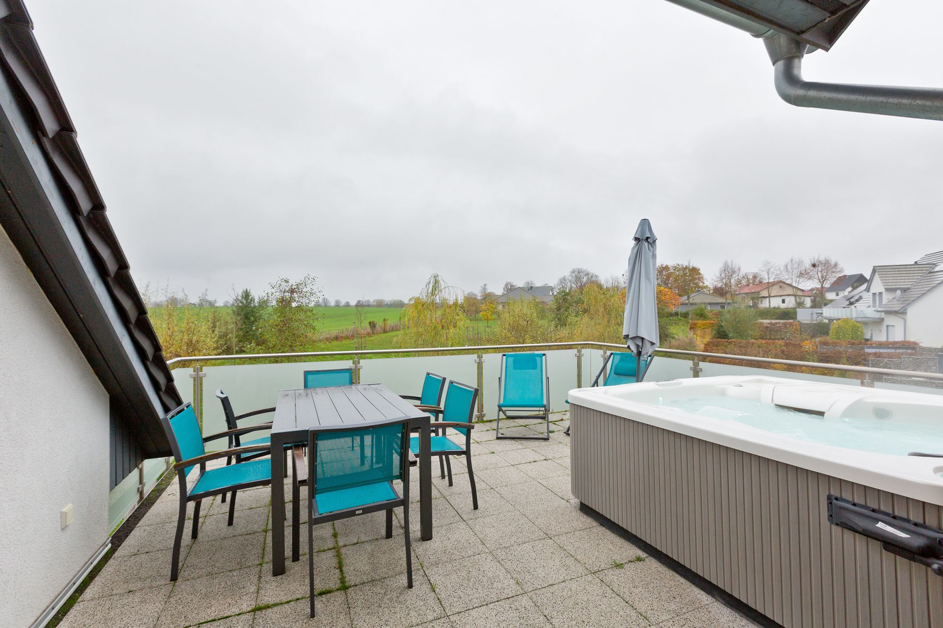 Terrasse mit Tisch, Stühlen, Whirlpool und Ausblick auf Felder und Häuser.