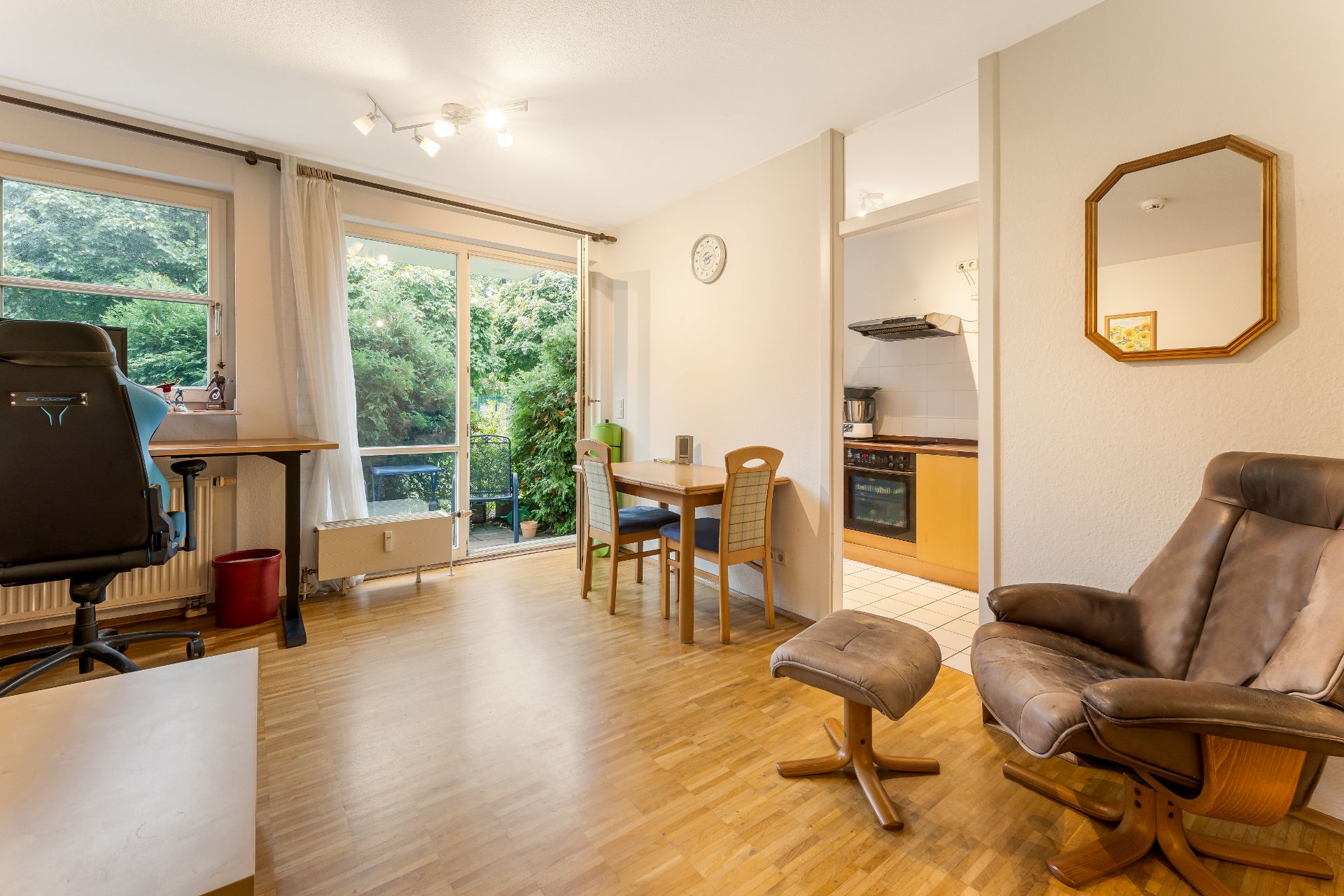Helles Wohnzimmer mit Schreibtisch, Essbereich, Sessel und Zugang zur Küche und Terrasse.