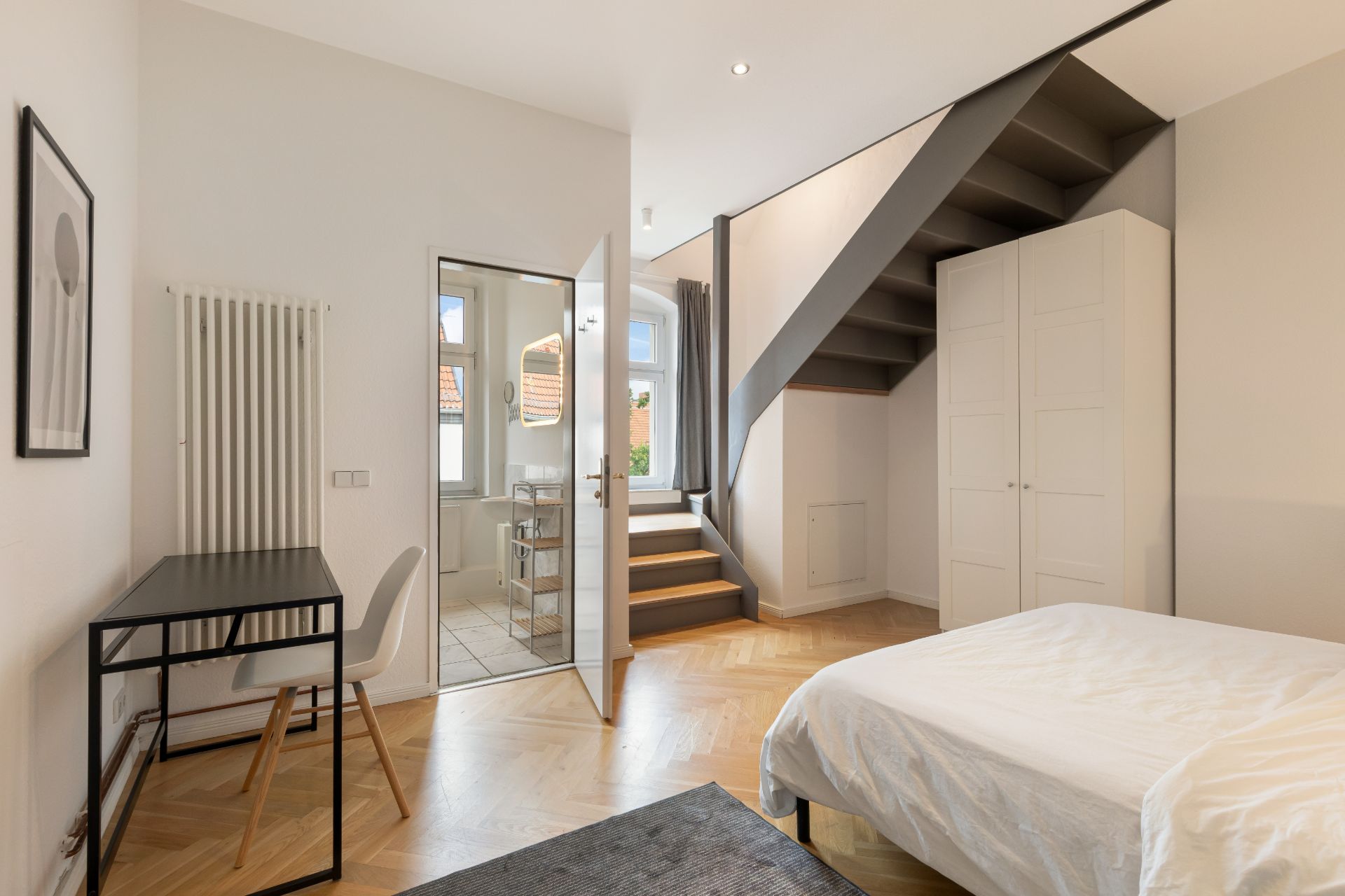 Modernes Schlafzimmer mit Schreibtisch, Bett, Kleiderschrank, Treppe und Zugang zum Bad.
