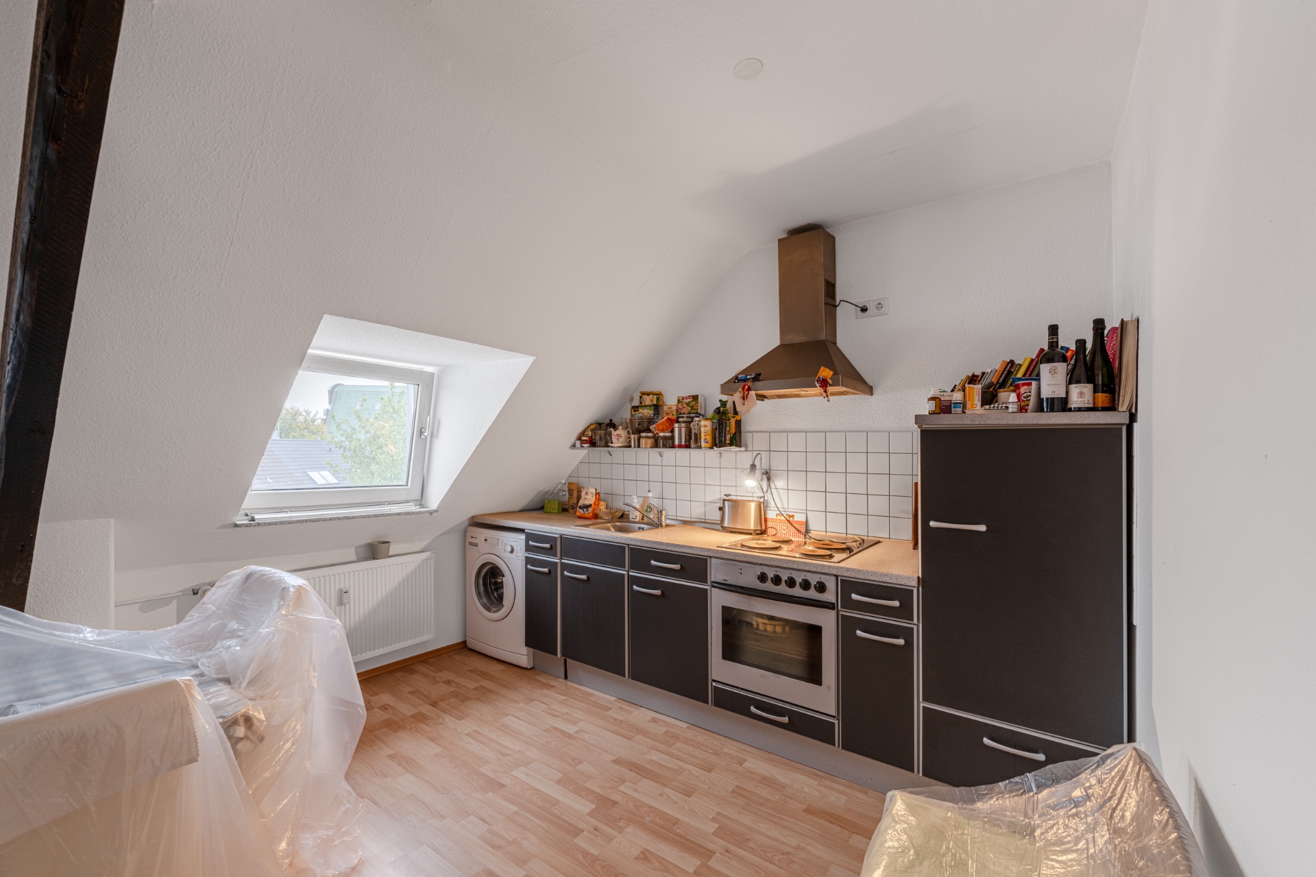 Küche mit Dachschräge, Fenster, schwarzer Küchenzeile, Waschmaschine und Herd.