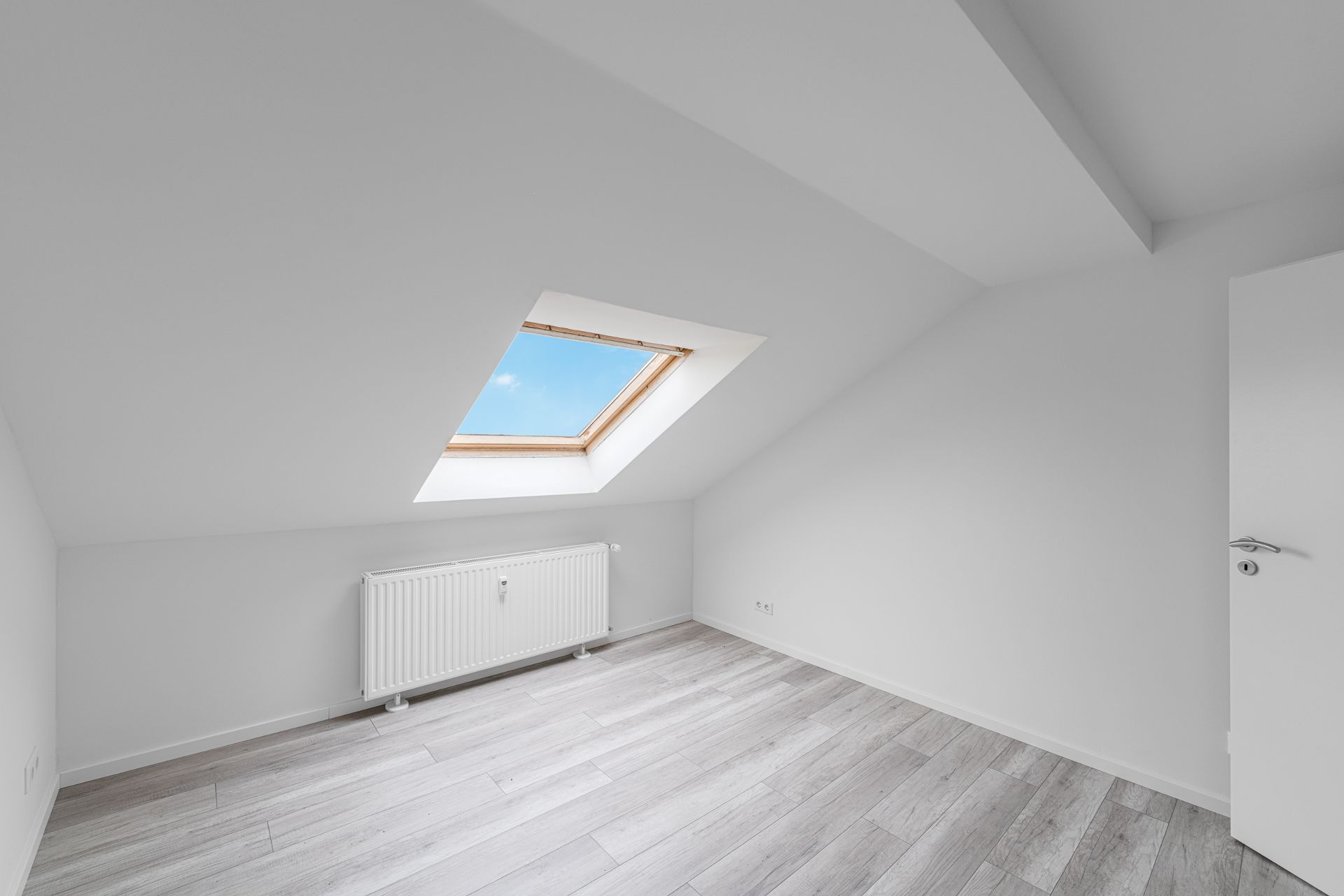 Heller Raum mit Dachfenster, Heizung und hellem Holzfußboden.