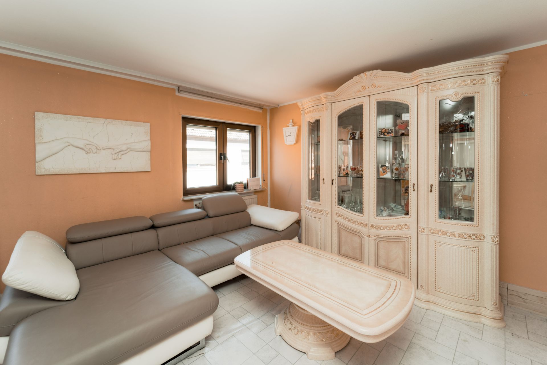 Wohnzimmer mit großer Eckcouch, Glastisch und weißem Vitrinenschrank vor orangefarbener Wand.