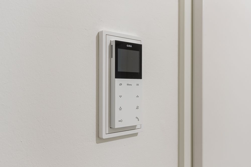 Weißes Bedienfeld mit Display und Tasten an einer Wand montiert.