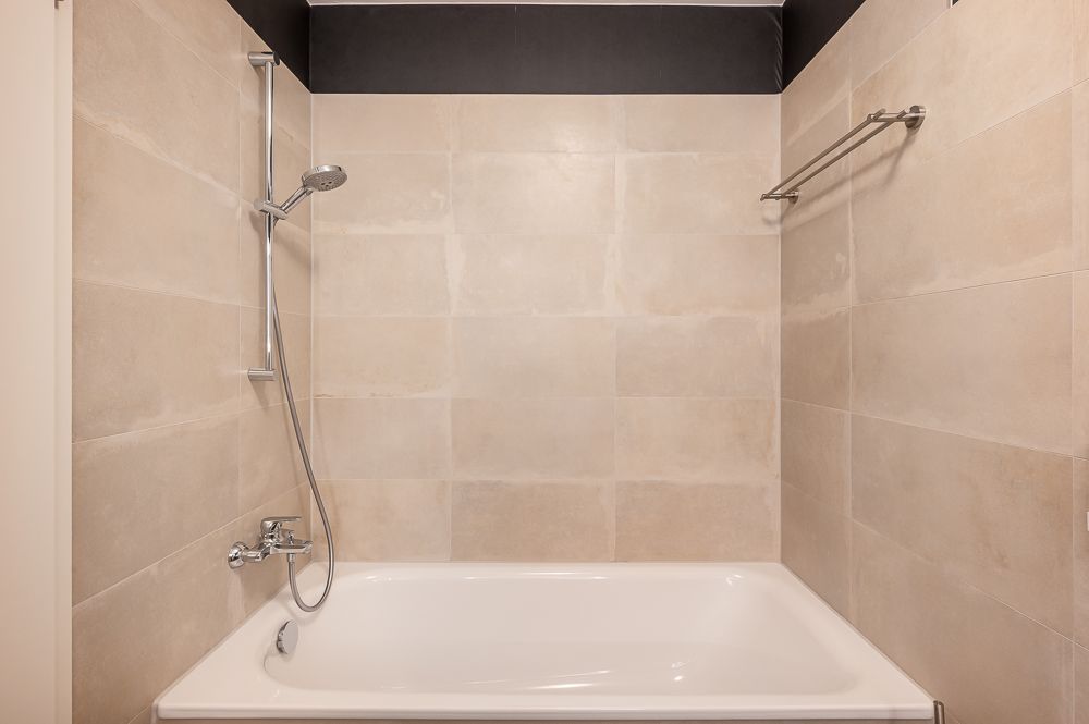 Badewanne mit Duschkopf und Handtuchhalter in einem hell gefliesten Badezimmer.