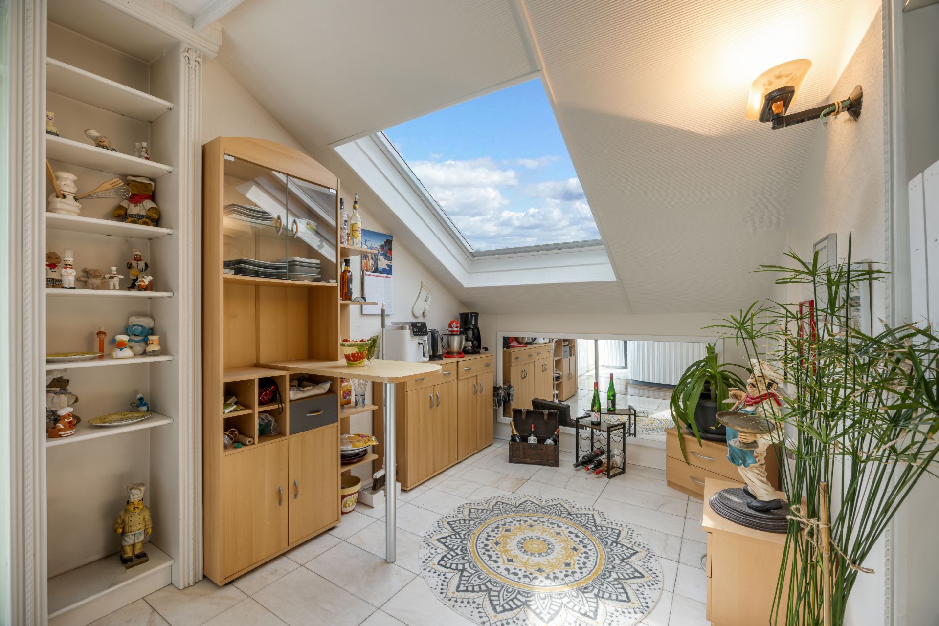Heller Raum mit Dachfenster, Regalen, Sideboards und buntem Fliesenmuster auf dem Boden.