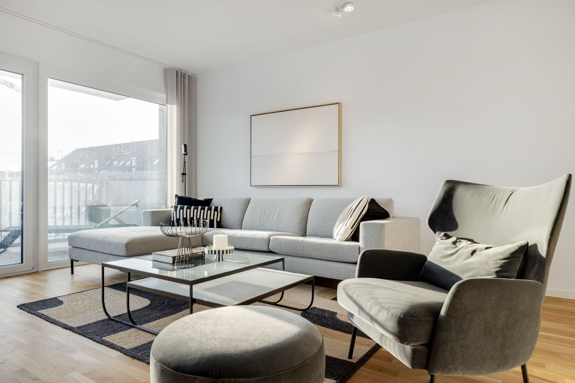 Helles Wohnzimmer mit grauem Sofa, Sessel, Couchtisch und großem Fenster.