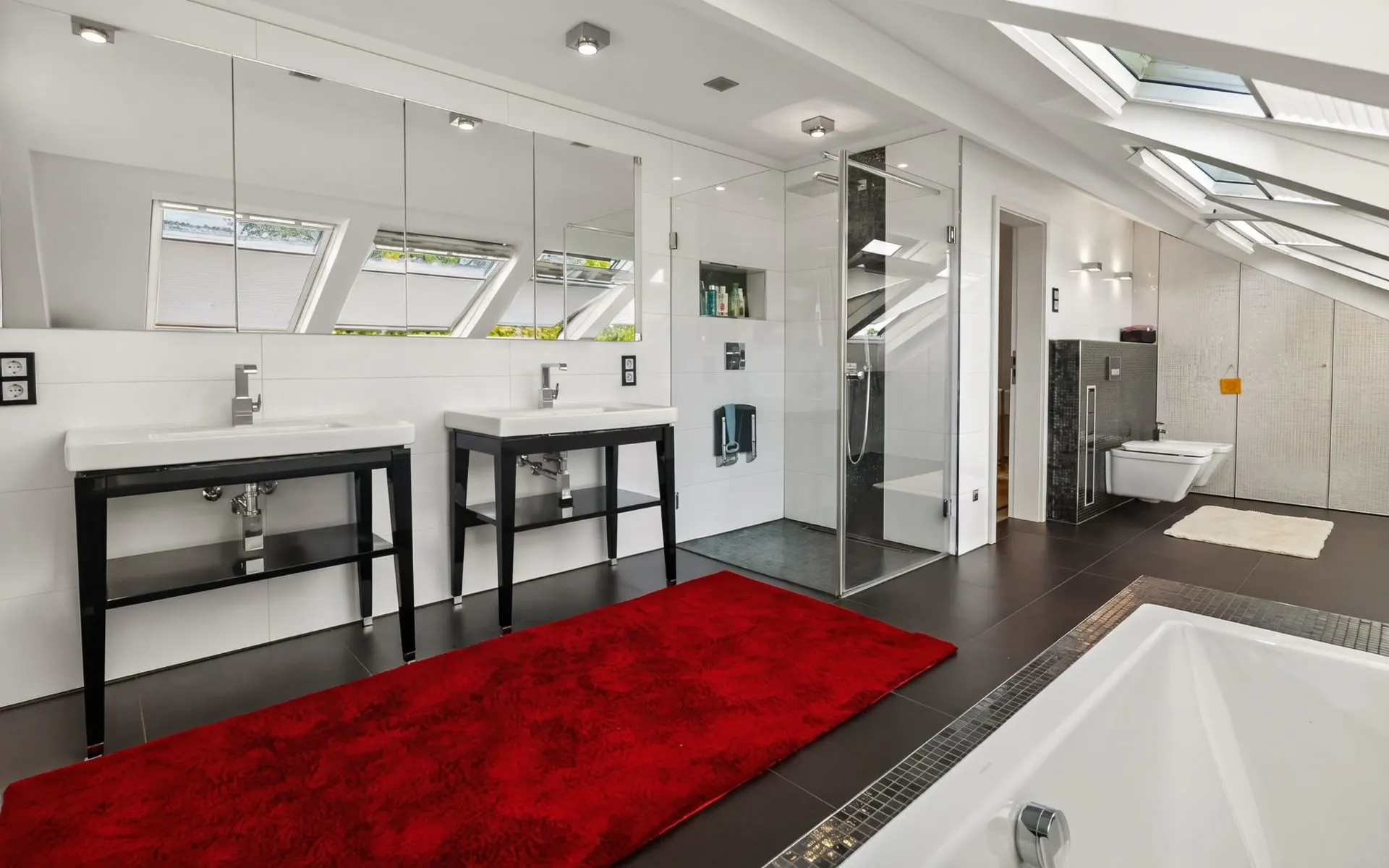 Modernes Badezimmer mit zwei Waschbecken, rotem Teppich, großer Dusche und Badewanne unter Dachfenstern.