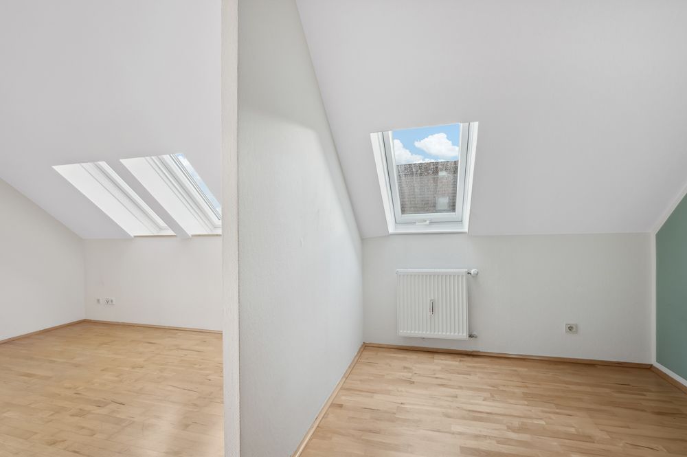 Heller Dachraum mit Holzfußboden, Dachfenstern und weißer Wandtrennung.