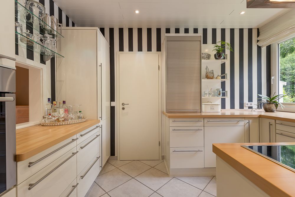 Moderne Küche mit weißen Schränken, Holzarbeitsplatten und schwarz-weiß gestreifter Wand.